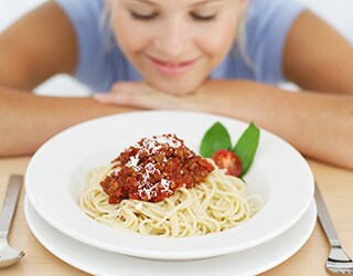 A woman smiling in front of a plate of spagetti and meatballs