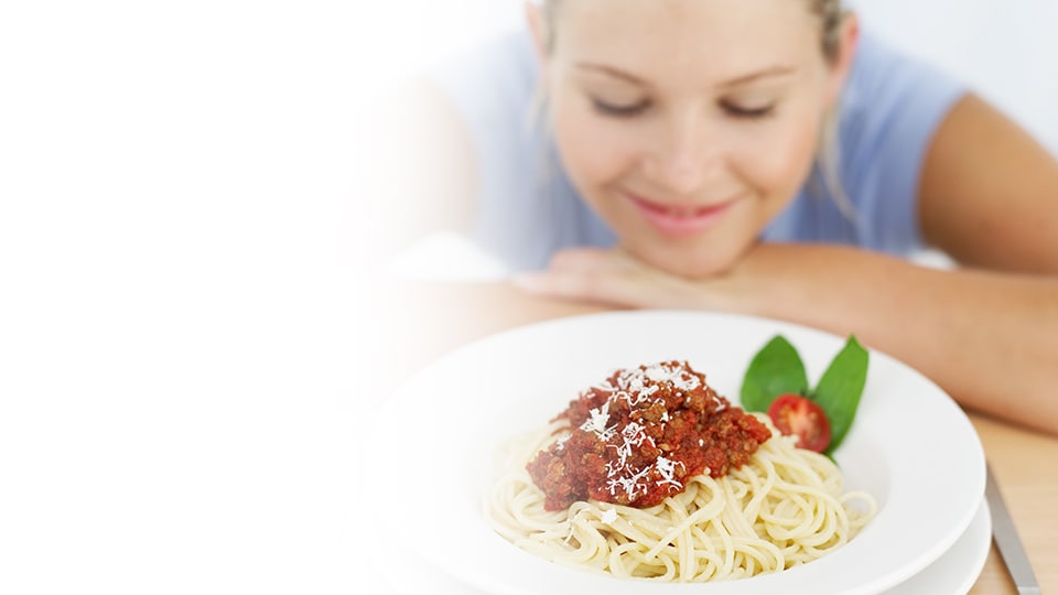 A woman smiling in front of a plate of spagetti and meatballs
