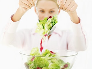 Stock image of woman lifting salad from a bowl into the air