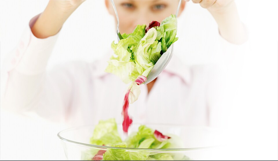 Stock image of woman lifting salad from a bowl into the air
