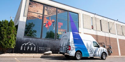 A truck with a vehicle wrap is in front of a building with a large window wrap, and each has strong graphics.
