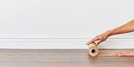 Person covering wood floor with rosin paper to protect floor.
