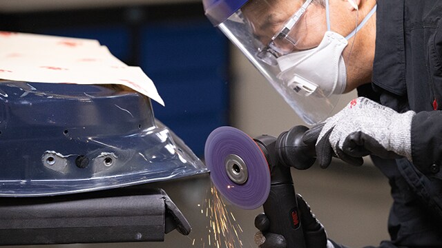 Worker using a 3M abrasive disc on metal while wearing safety gear.
