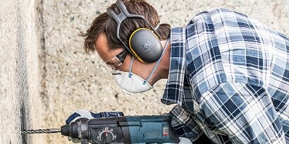 Man wearing 3M safety helmet and mask drilling a wall

