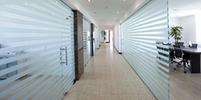 A long office hallway with glass walls has striped wall wraps that provide privacy and a sleek look.
