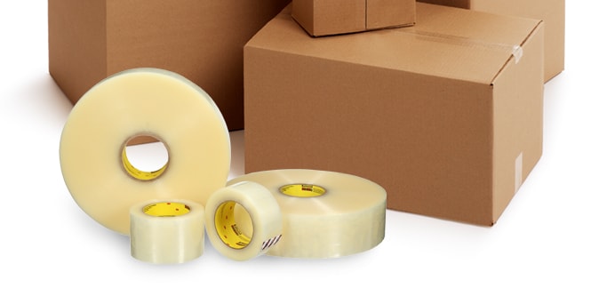 Four rolls of clear tapes of different sizes in front of cardboard boxes.
