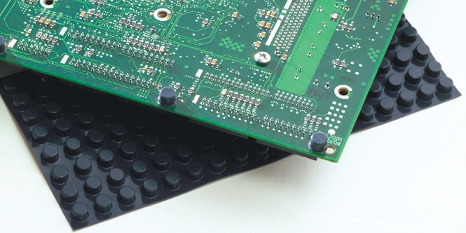 Close‑up of a circuit board on top of a sheet of Bumpon Rubber Pads.
