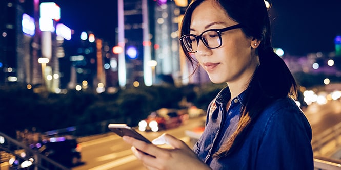 Image of a woman using her mobile device in a city at night.
