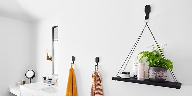 A Wall in a bathroom with 3M CLAW™ Plasterboard Hooks hanging a plant, and towels on the wall.
