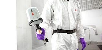 Person in a white protective paint suit using a 3M™ Performance Spray Gun.
