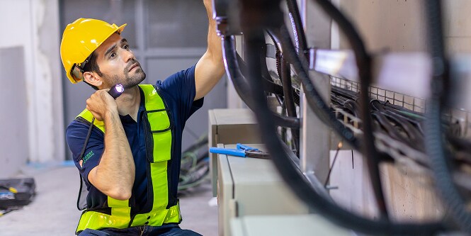 Worker in safety gear looking at electrical connections with a flashlight
