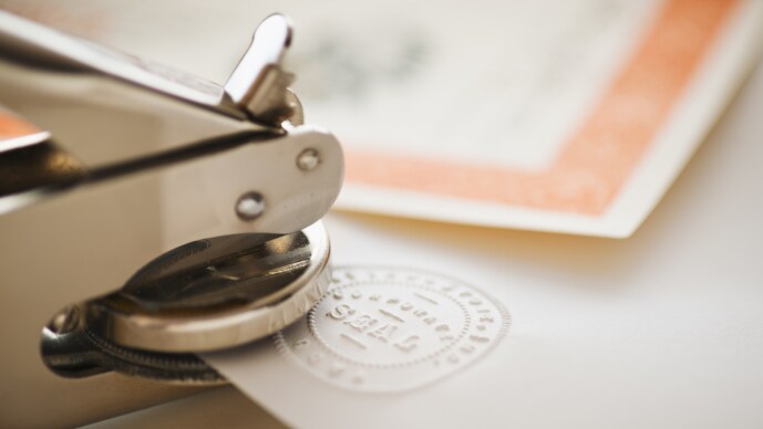 Handheld embosser creating a raised seal on an official document.
