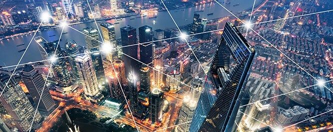 City skyline with a graphical overlay of nodes of light connected by straight lines creating a geometric pattern.
