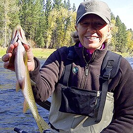 Jean Sweeney in a boat on the water, holding a fish