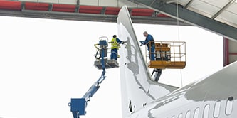 Two people in risers working on the tail of a plane.