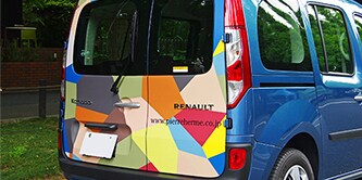 Rear of a delivery van displaying a colorful partial vehicle wrap.
