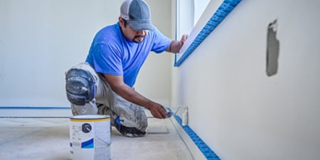  A professional painter painting a wall and using ScotchBlue™ PROSharp™ Masking Tape to achieve clean, precise edges.
