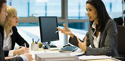 People talking at a desk over a computer monitor
