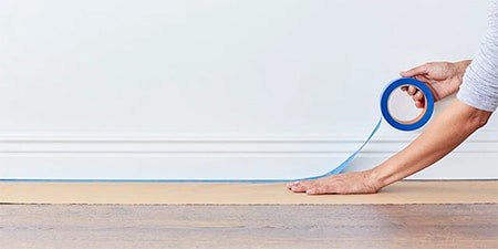 Person using 3M masking tape to hold down rosin paper to protect wood floor
