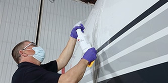 Person with a mask using 3M™ Surface Pre-Treatment AC-131 on an aircraft.
